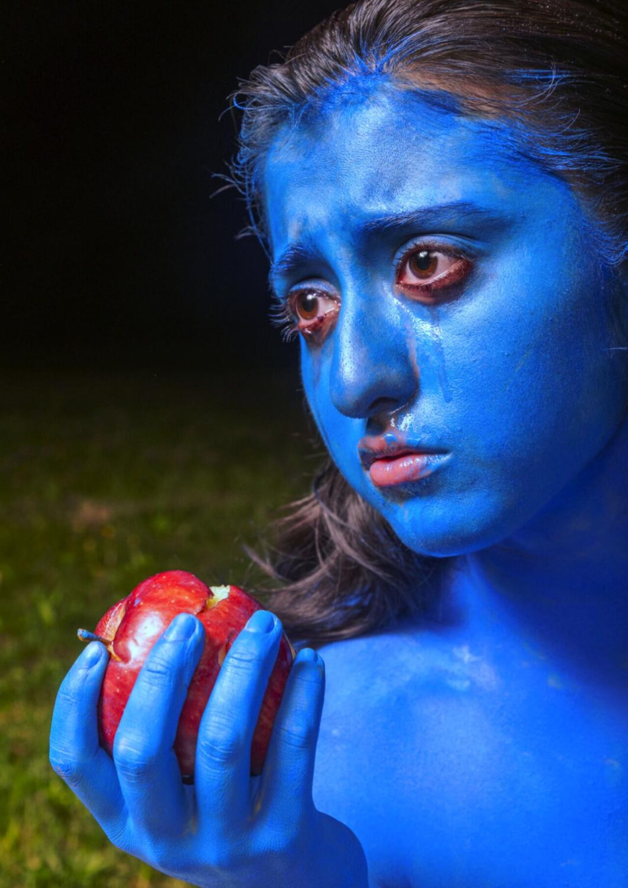 person in blue holds apple with bite taken out and cries